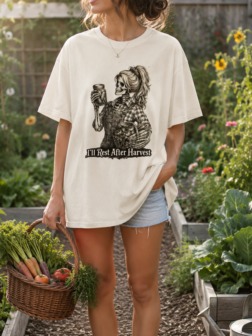 Person standing in a garden holding a basket of vegetables, wearing a white t-shirt with a graphic design.